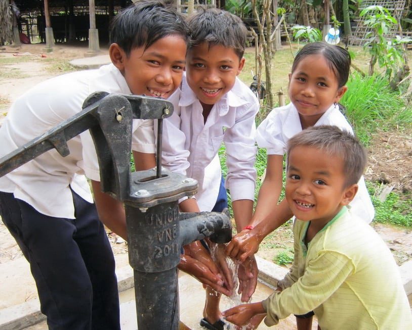an image of four young children in a foreign country washing their hands from a clean water spout in their village