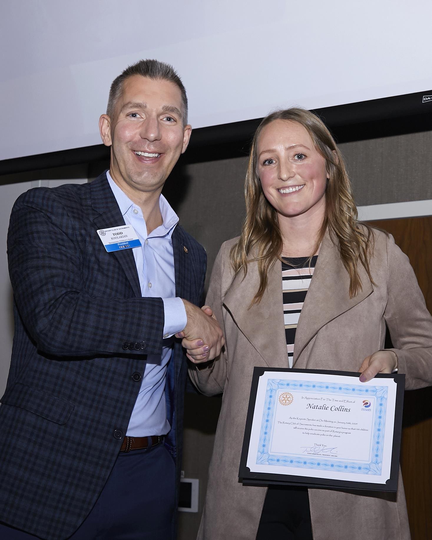 2 people smiling and shaking hands while 1 holds an award