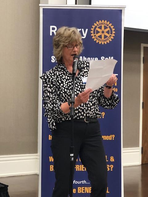 person speaking into a microphone while holding a paper in their hands and a rotary banner behind them