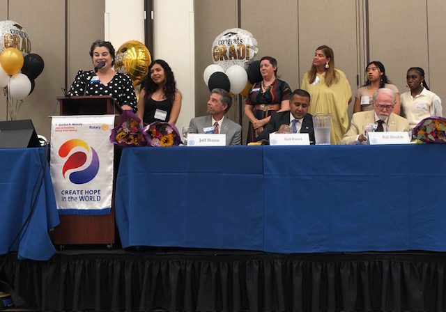 10 people looking at a stage looking at someone speaking into a microphone