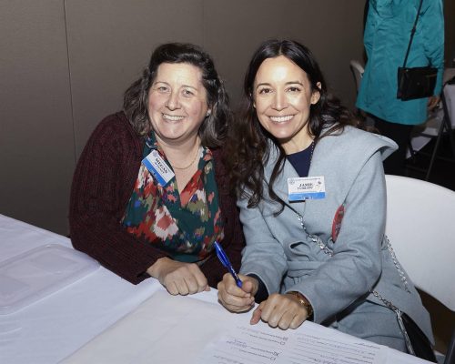 two people sitting at desk smiling at camera