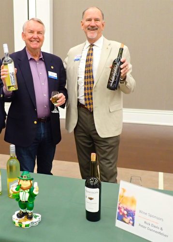 two people holding up wine bottles by table