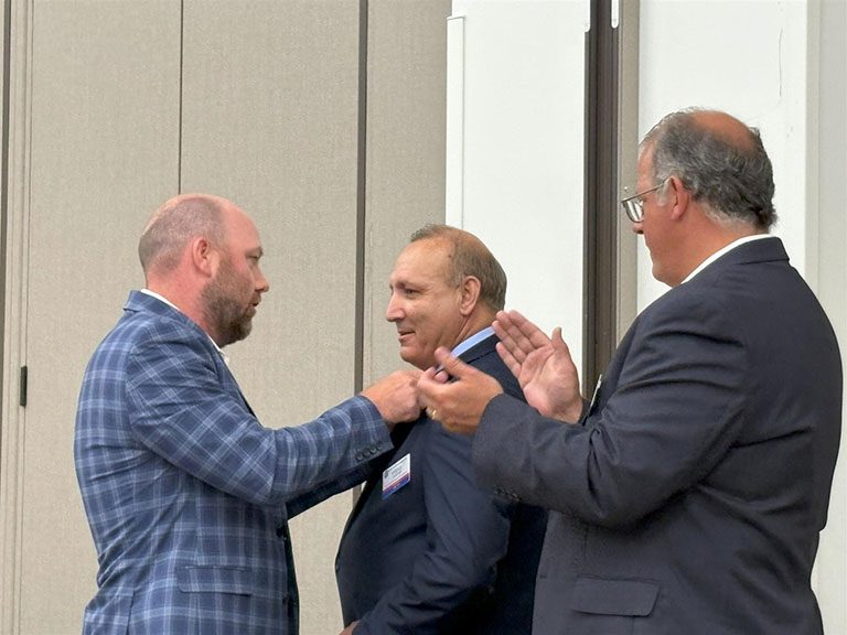 Bobby putting badge on a person while the guy next to it clapping.
