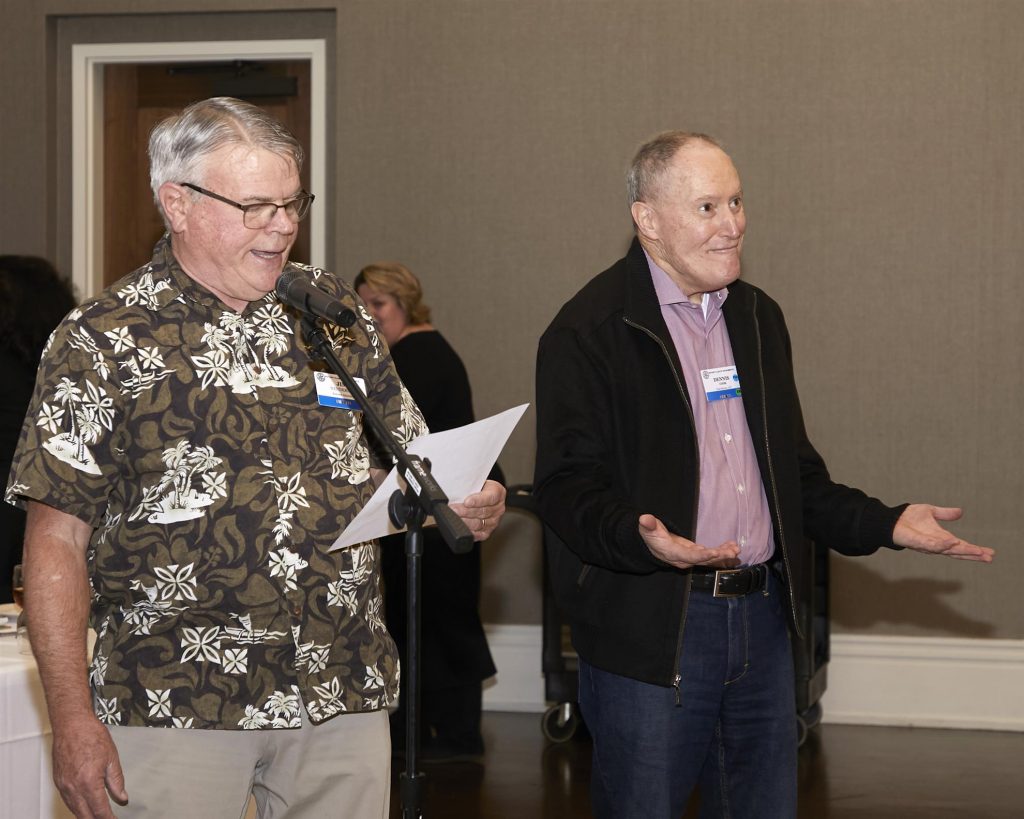 Two men standing next to each other while one is speaking into a microphone