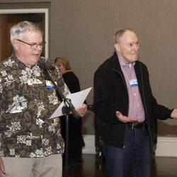 Two men standing next to each other while one is speaking into a microphone