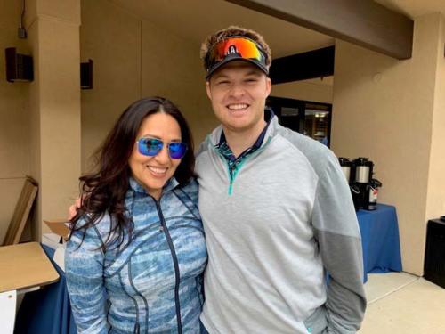 A woman and man wearing athletic wear jackets and sunglasses smile at the camera