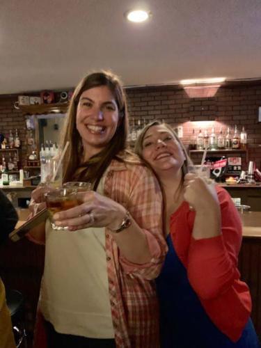 Two women pose with drinks in a bar.