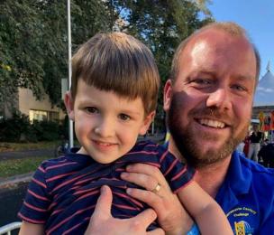 A man lifts his young son up to smile at the camera