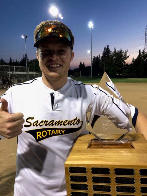 A young man in a Sacramento Rotary team shirt poses with a softball trophy and a thumbs up