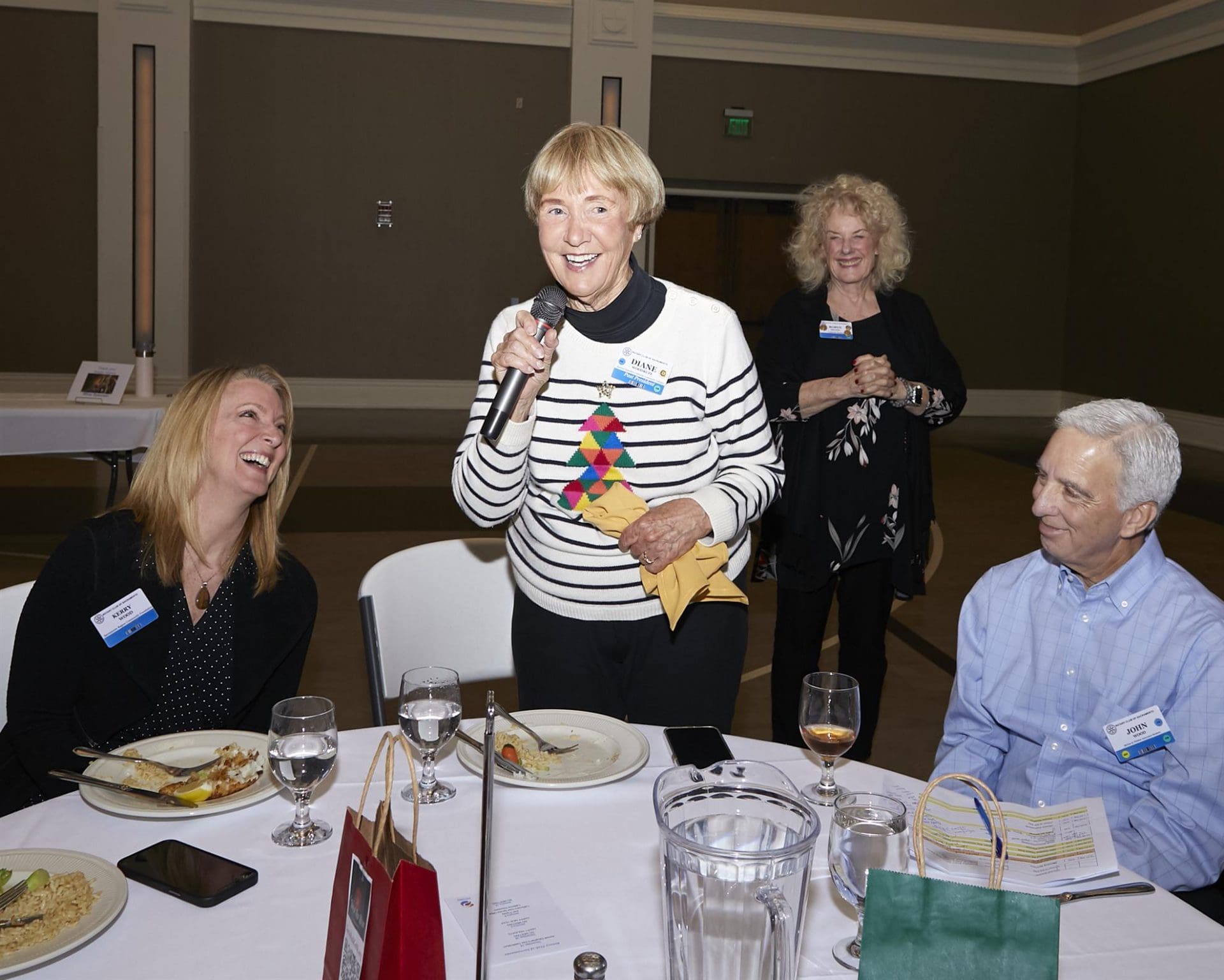 Diane speaking into microphone as others stand and sit around her
