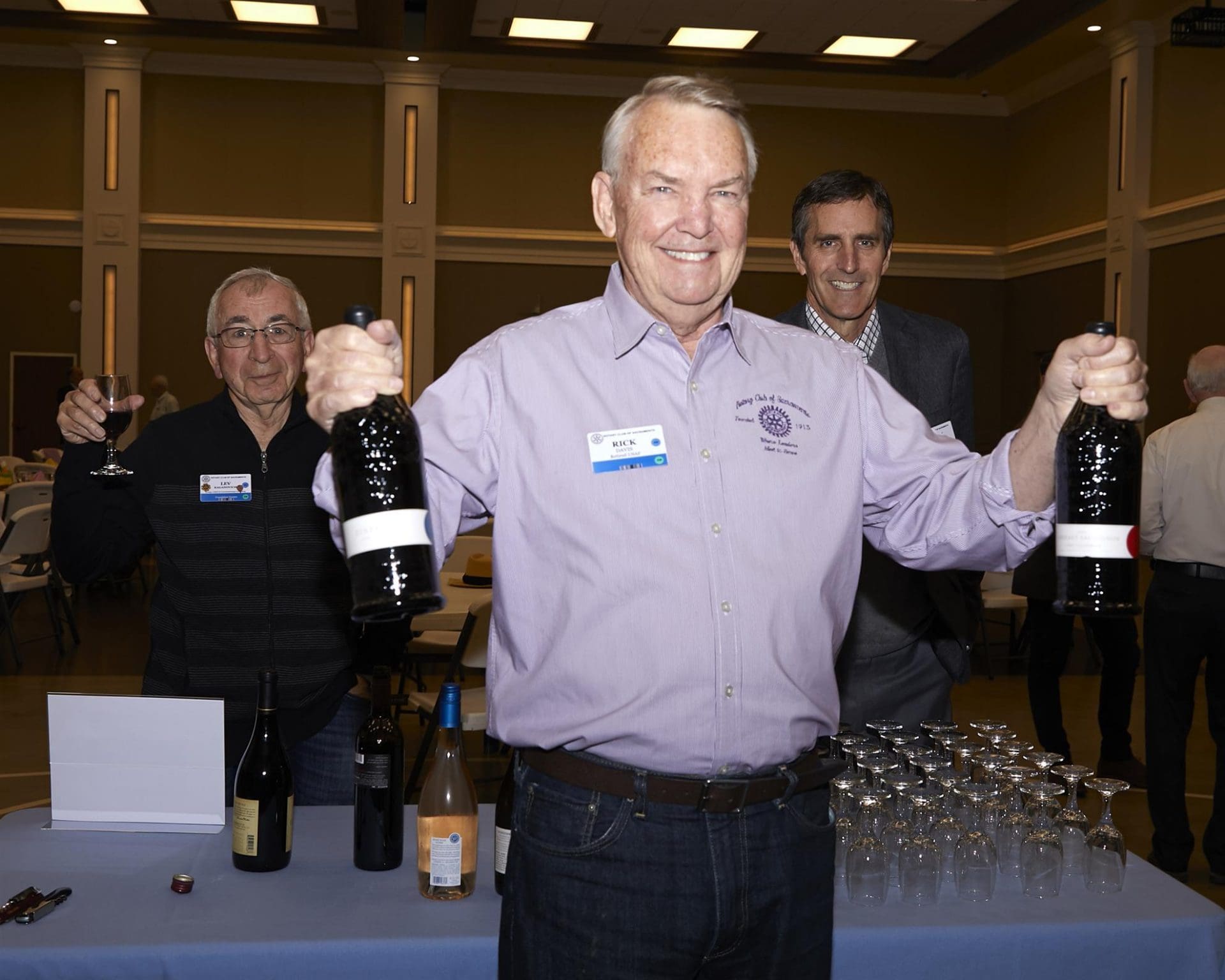 person smiling and holding up 2 bottles while 2 people behind him smile