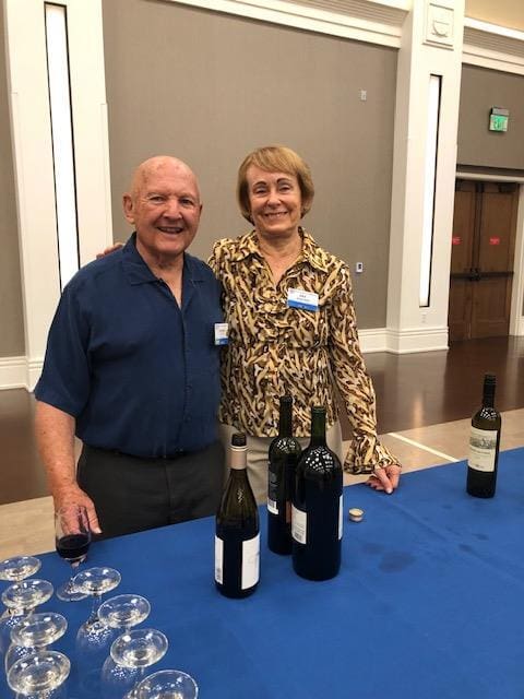 2 people smiling with bottles and glasses in front of them