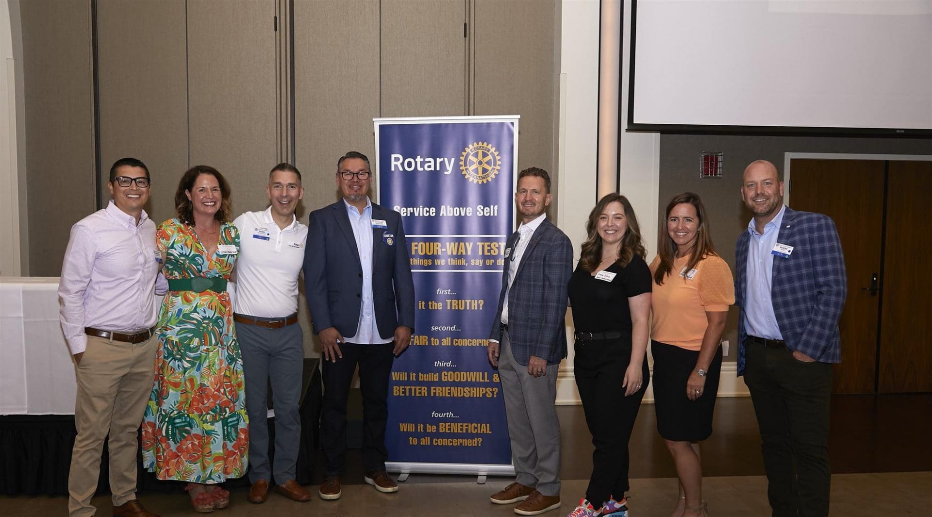 4 people to the left and 4 people to the right of a rotary club banner smiling
