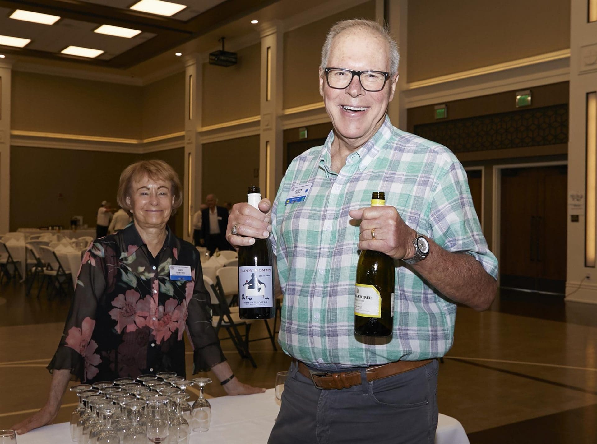 2 people smiling while 1 holds up 2 bottles