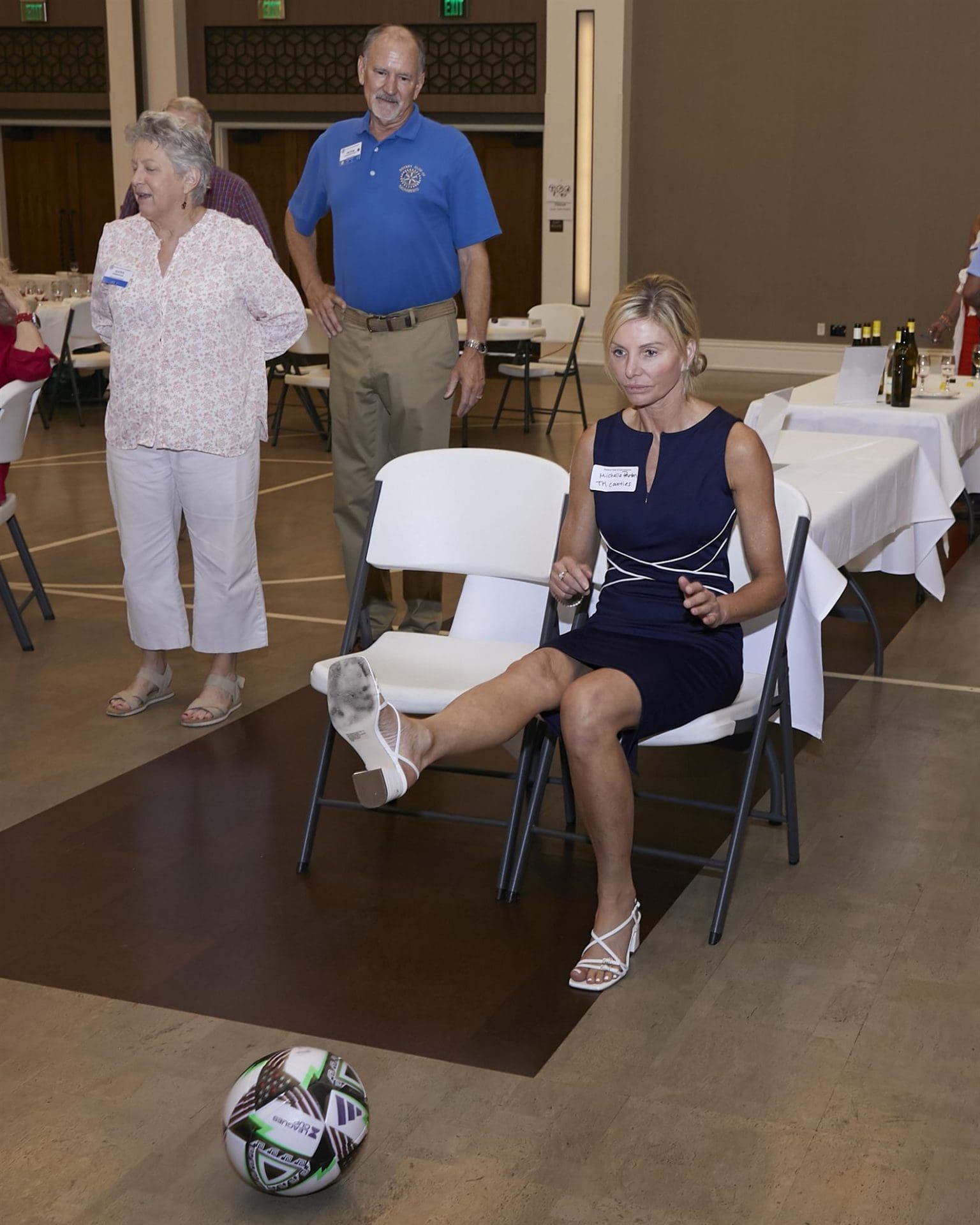 person kicking a soccer ball while sitting on a chair and 3 other people looking at them