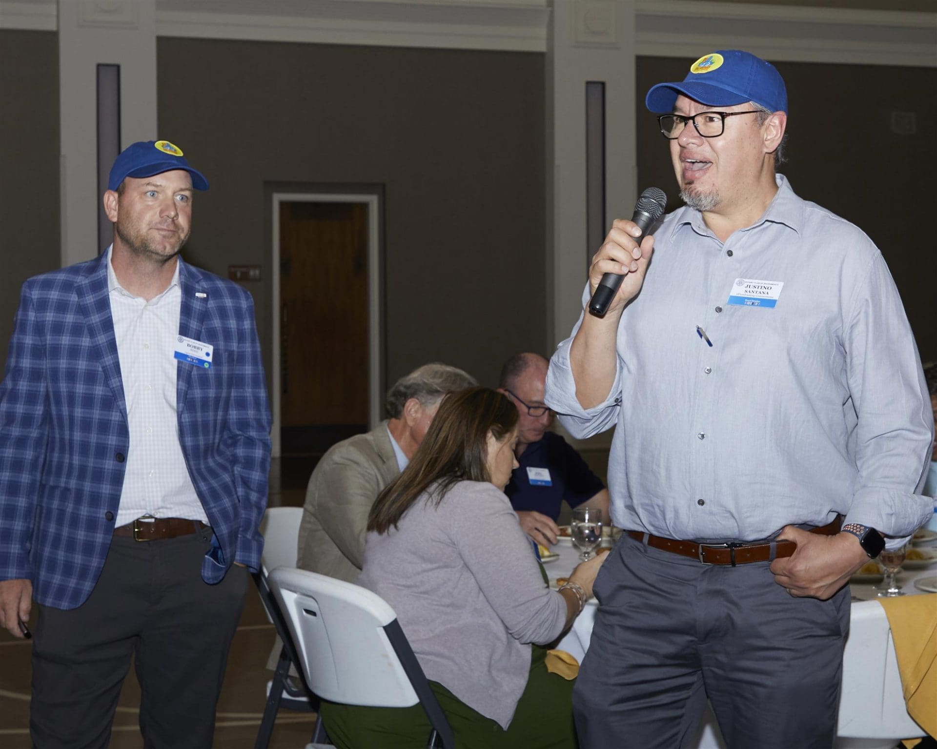 person holding microphone speaking to people while another person looks at them