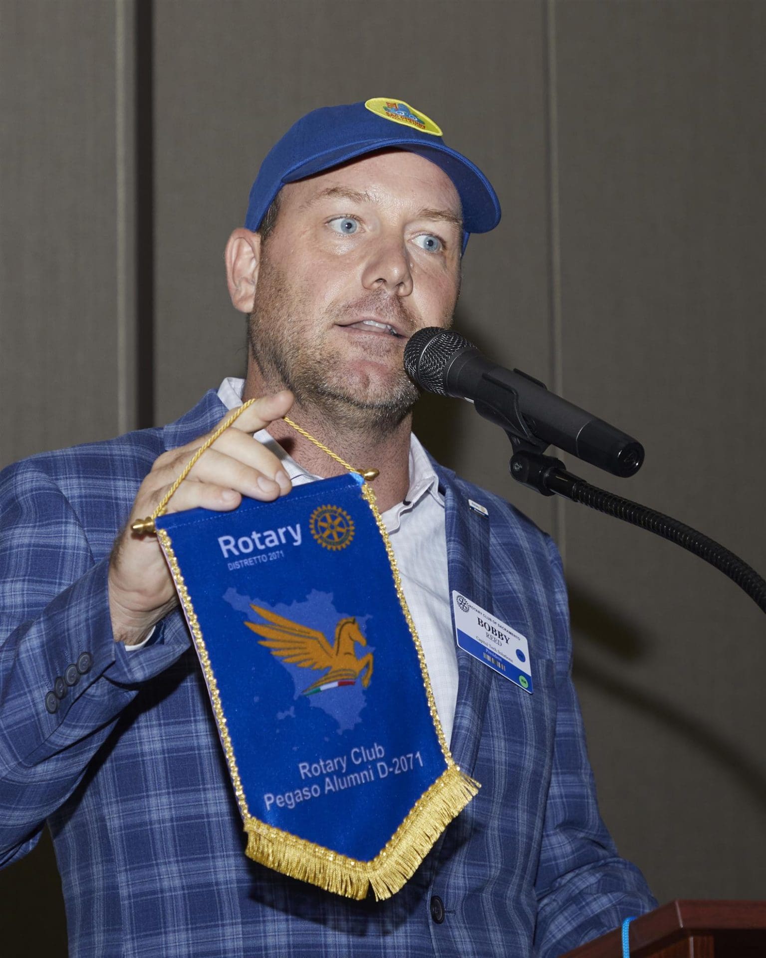 person speaking into microphone while holding rotary club sign