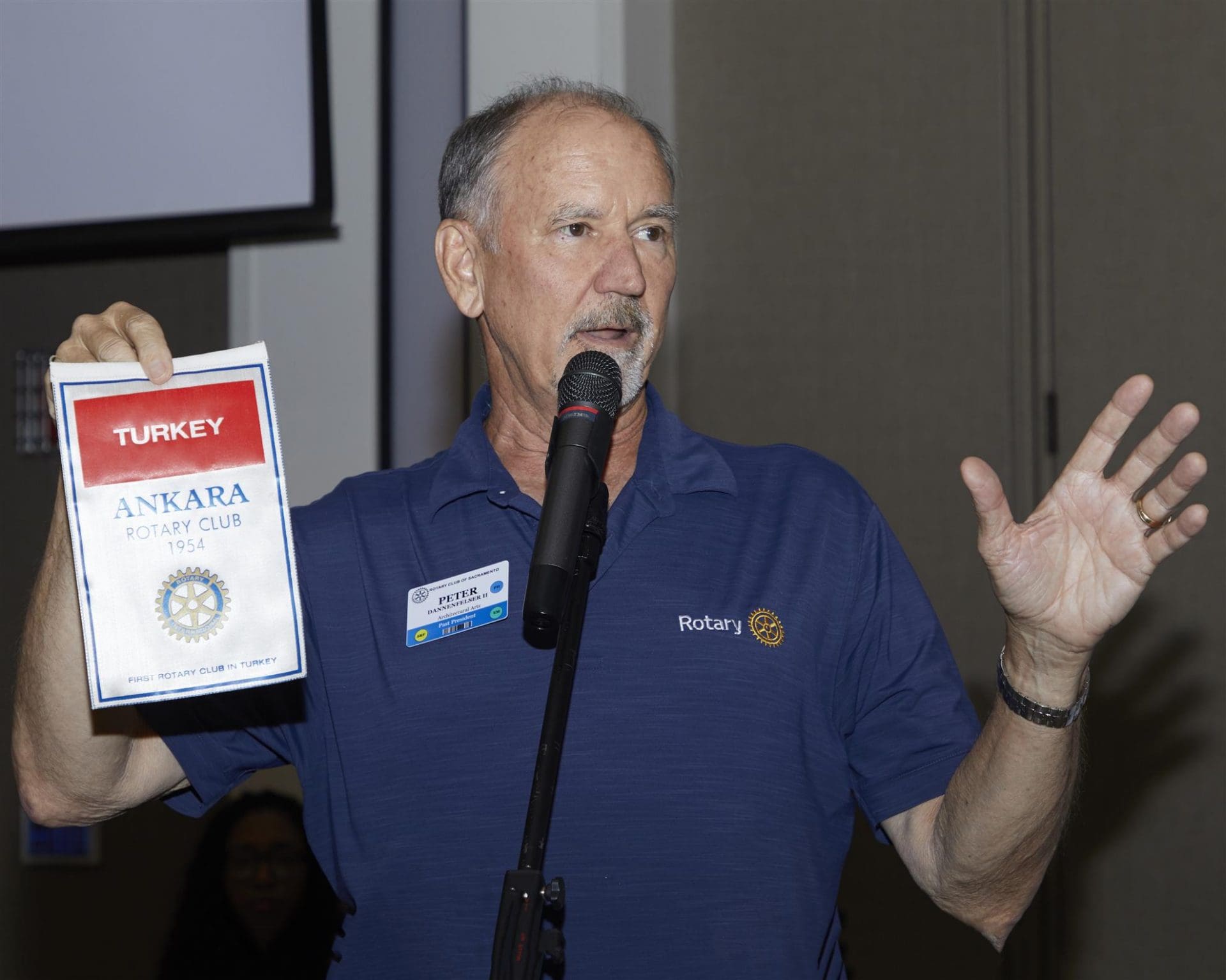 person speaking into a microphone and holding a turkey ankara rotary club paper