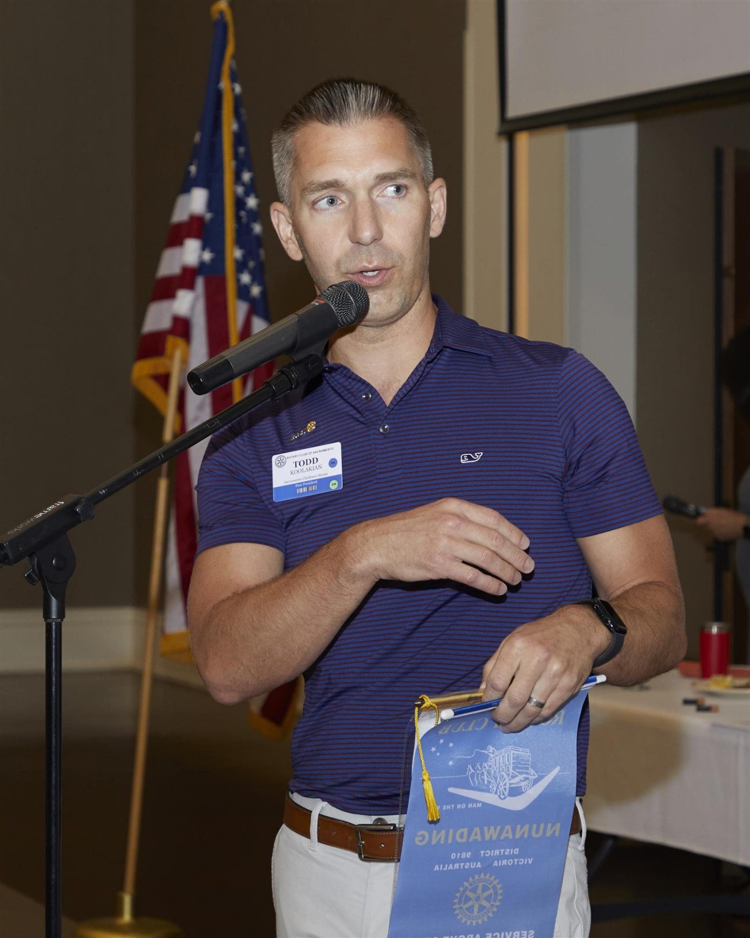 person speaking into microphone and holding rotary club paper