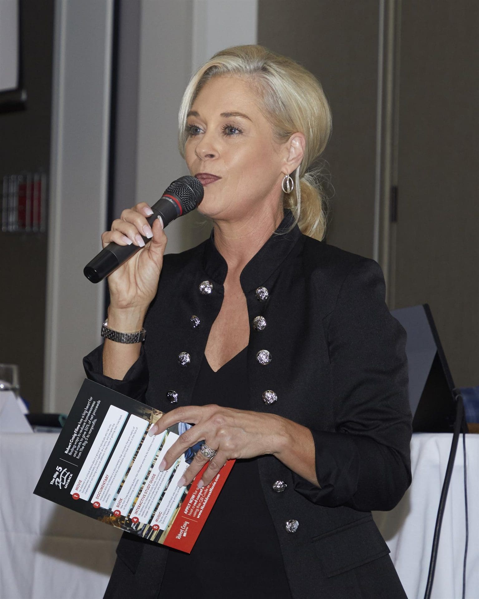 person speaking into microphone and holding rotary club paper