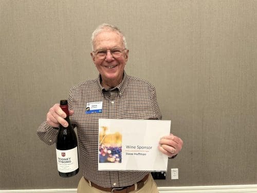 man holding up a wine sponsor paper and a wine bottle