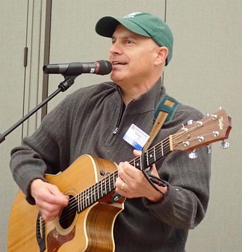 person speaking into microphone and playing guitar