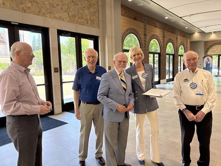 Group of five smiling at the camera at the entrance of the building