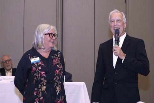 Two older rotary members standing together and speaking into microphones