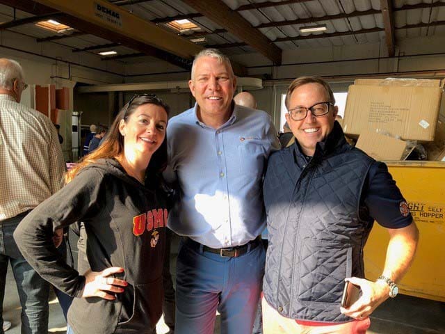 Three people smile at the camera in a warehouse